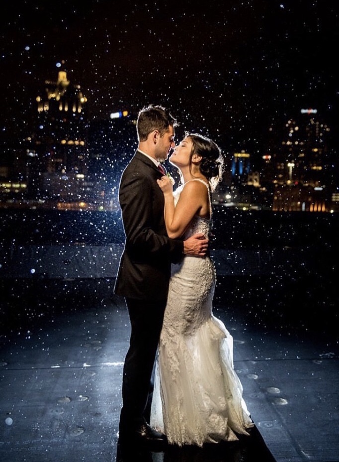 color photo of the bride and groom embracing in a dance pose and about to kiss. It is night time and the raindrops around them are illuminated by the flash.