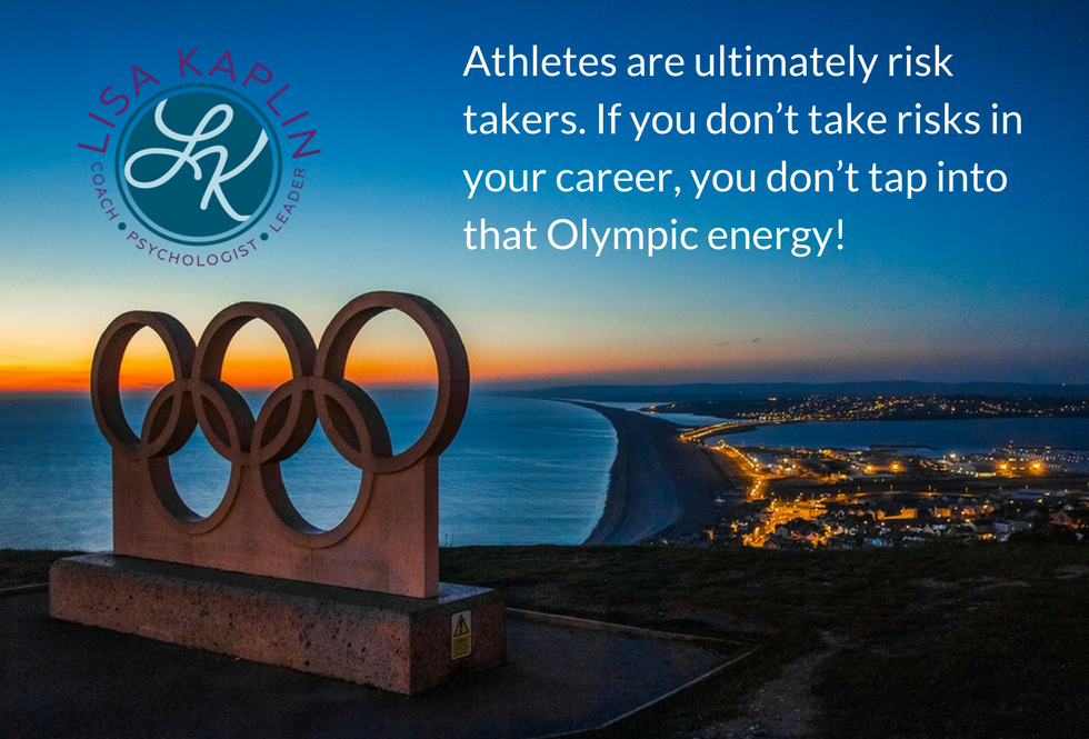 photo of the olympic rings on a hill overlooking the water and the lights of a city taken at sunset