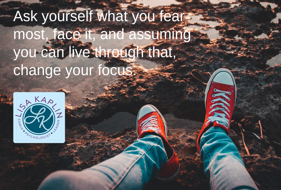 A color photo of a person’s legs and feet dangling over muddy ground. The person is wearing jeans and red converse all stars. At the top left of the photo is the text “Ask yourself what you fear most, face it, and assuming you can live through that, change your focus.” The Lisa Kaplin logo is beneath the text.