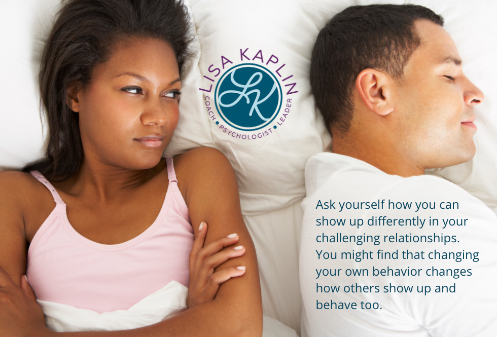 A color photo of a Black woman and a white, possibly Latinx man lying in bed. The man is asleep and the woman is staring at him angrily. The text at in the bottom right corner reads “Ask yourself how you can show up differently in your challenging relationships. You might find that changing your own behavior changes how others show up and behave too.” The Lisa Kaplin logo is centered in between the couple.