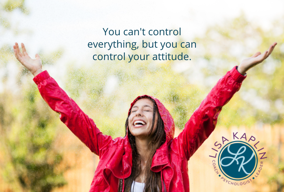 A color photo of a white woman wearing a red rain jacket. She is standing in the rain with her arms outstretched to the sky. She is smiling and looking up with her eyes closed. The text above her head reads “You can't control everything, but you can control your attitude.” The Lisa Kaplin logo is in the bottom right corner.