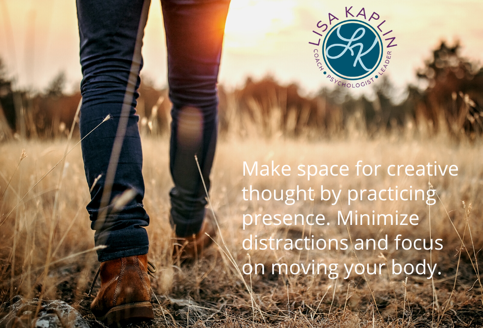 A color photo of a the back of a person’s legs and feet as they walk through a field. They are wearing jeans and hiking boots. The light is a golden sunset. The text in the bottom right of the image reads “Make space for creative thought by practicing presence. Minimize distractions and focus on moving your body.” The Lisa Kaplin logo is above the text.