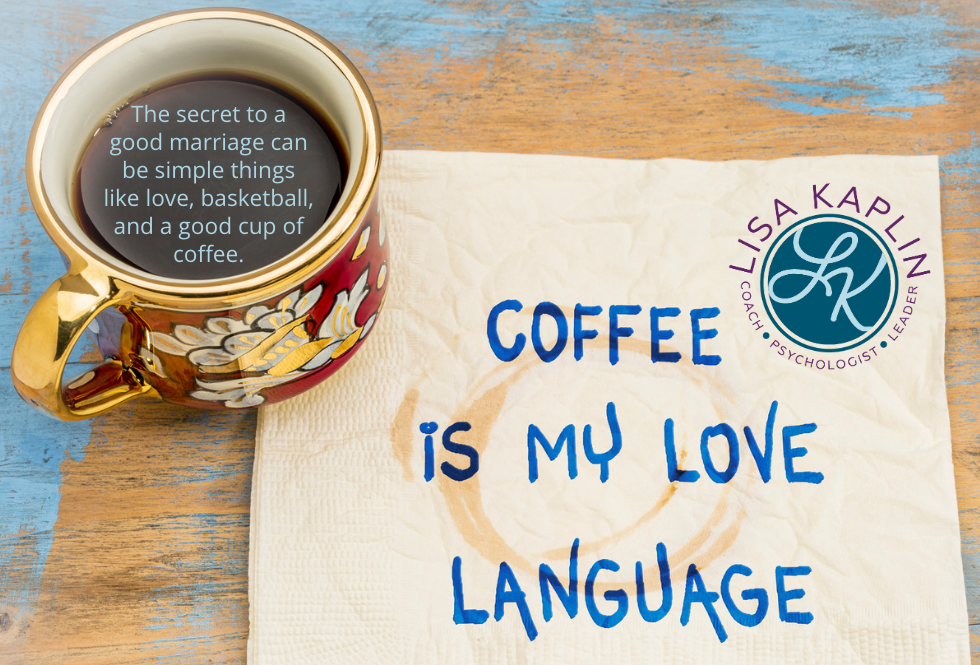 A color photo of a a cup of coffee sitting on a wooden table painted in a faded sky blue color. Next to the cup is a coffee-stained napkin on which someone has written “coffee is my love language.” The text floating in the coffee in the cup reads “The secret to a good marriage can be simple things like love, basketball, and a good cup of coffee.” The Lisa Kaplin logo is in the upper right corner of the napkin.